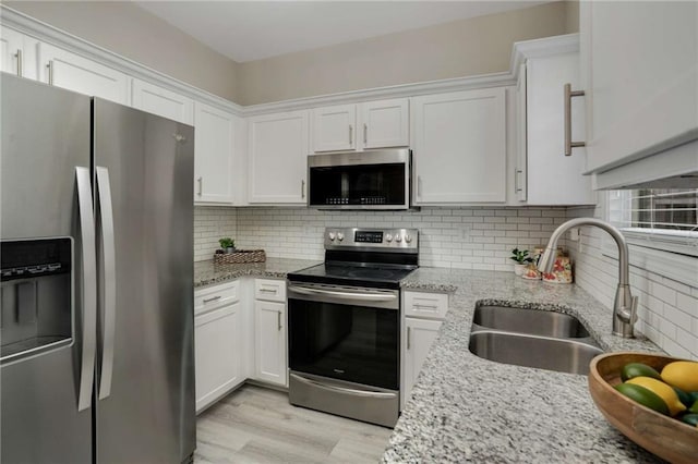 kitchen featuring light stone counters, stainless steel appliances, a sink, white cabinets, and tasteful backsplash