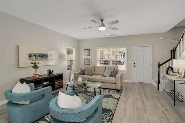 living room featuring light wood-style floors, a ceiling fan, baseboards, and stairs