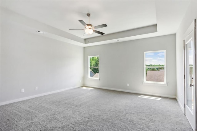 empty room featuring a tray ceiling, ceiling fan, and carpet