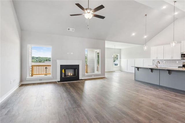 unfurnished living room with high vaulted ceiling, sink, hardwood / wood-style floors, and ceiling fan