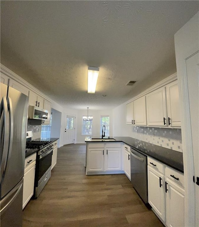 kitchen with kitchen peninsula, appliances with stainless steel finishes, white cabinets, and tasteful backsplash