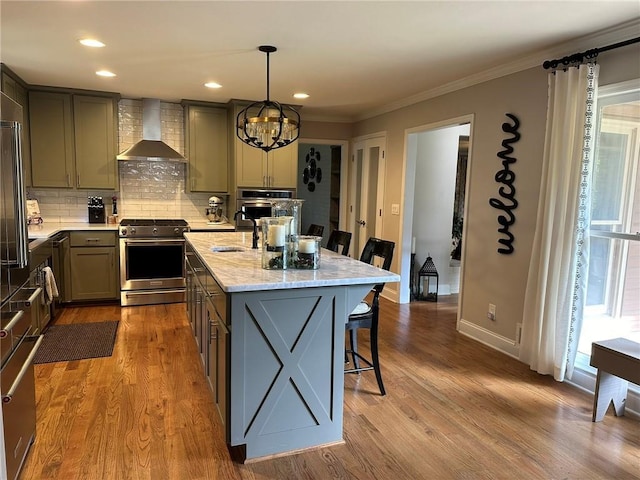 kitchen with decorative light fixtures, a center island with sink, light stone countertops, appliances with stainless steel finishes, and wall chimney exhaust hood