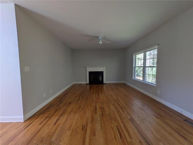 unfurnished living room with a ceiling fan, baseboards, a fireplace with flush hearth, and light wood finished floors
