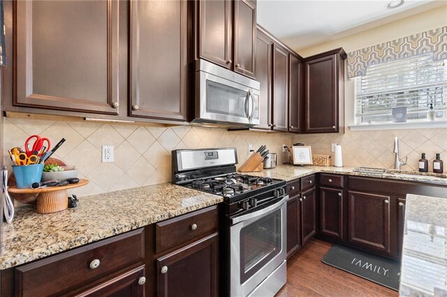 kitchen with stainless steel appliances, light stone counters, dark hardwood / wood-style floors, dark brown cabinets, and a kitchen island