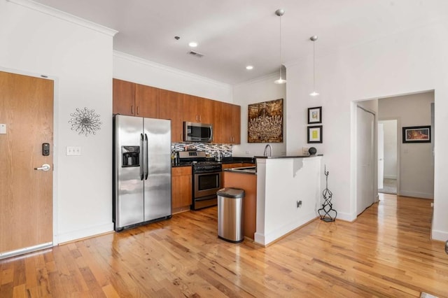 kitchen featuring crown molding, decorative light fixtures, kitchen peninsula, stainless steel appliances, and backsplash