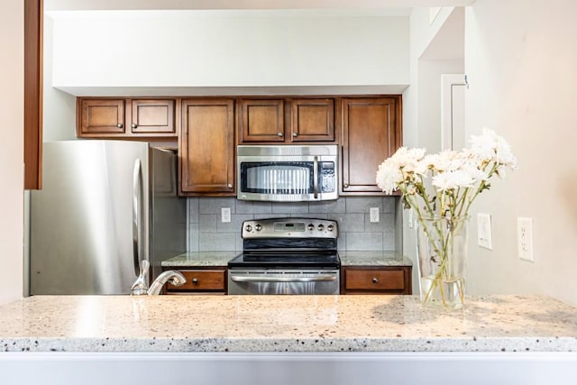 kitchen featuring decorative backsplash, light stone countertops, sink, and appliances with stainless steel finishes