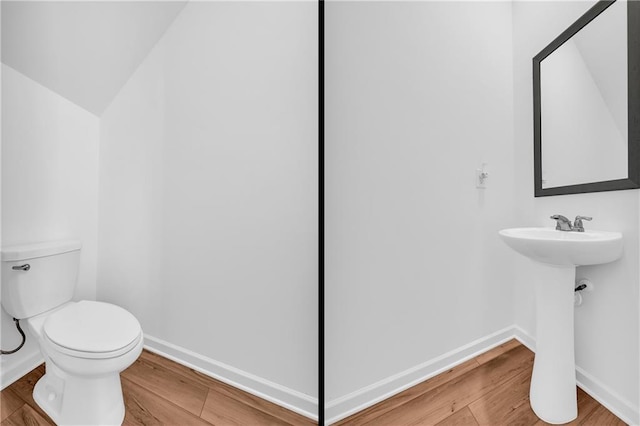 half bath with a sink, toilet, baseboards, wood finished floors, and vaulted ceiling