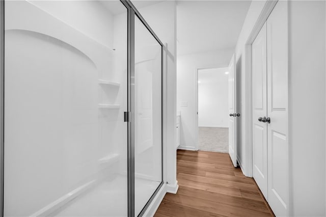bathroom with baseboards, wood finished floors, and a shower stall