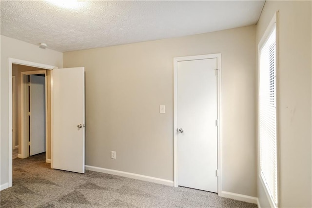 unfurnished bedroom featuring a textured ceiling, light colored carpet, and multiple windows