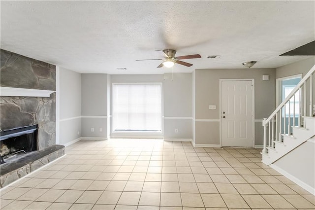 unfurnished living room featuring ceiling fan, a healthy amount of sunlight, a stone fireplace, and a textured ceiling