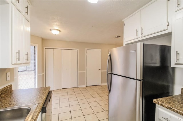 kitchen with light tile patterned floors, white cabinetry, stainless steel refrigerator, and dark stone counters