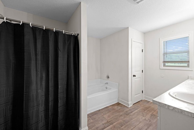 bathroom featuring vanity, wood finished floors, baseboards, a textured ceiling, and a bath