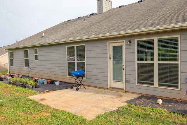 rear view of property featuring a yard, a patio, a chimney, and roof with shingles