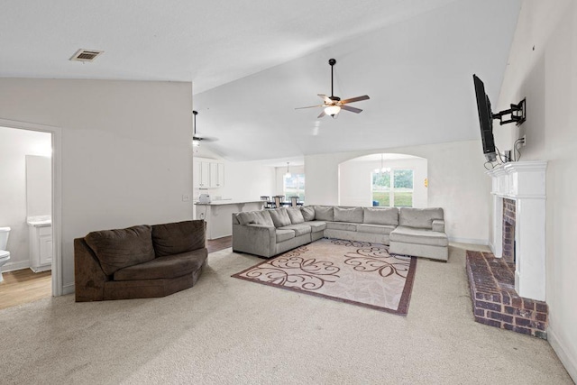 carpeted living room featuring a ceiling fan, visible vents, arched walkways, a brick fireplace, and high vaulted ceiling