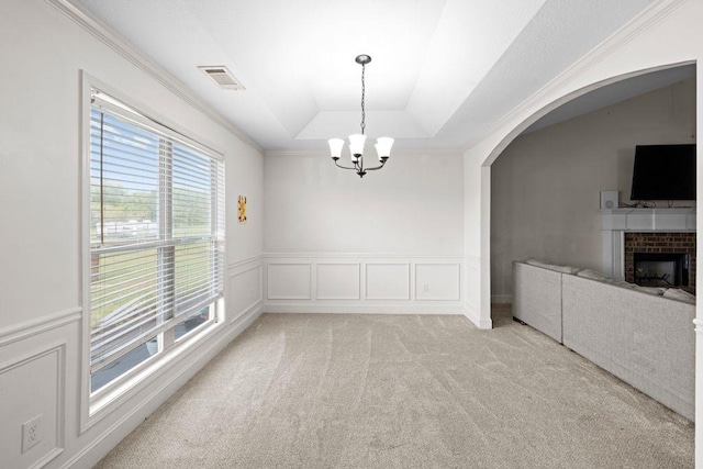unfurnished dining area featuring visible vents, light colored carpet, arched walkways, a fireplace, and a chandelier