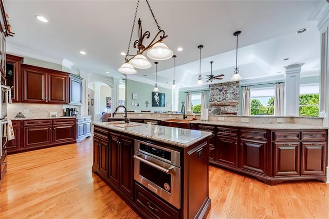 kitchen featuring stainless steel oven, tasteful backsplash, hanging light fixtures, a kitchen island with sink, and ornamental molding