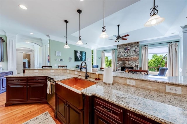 kitchen featuring light wood-type flooring, a stone fireplace, a raised ceiling, and pendant lighting