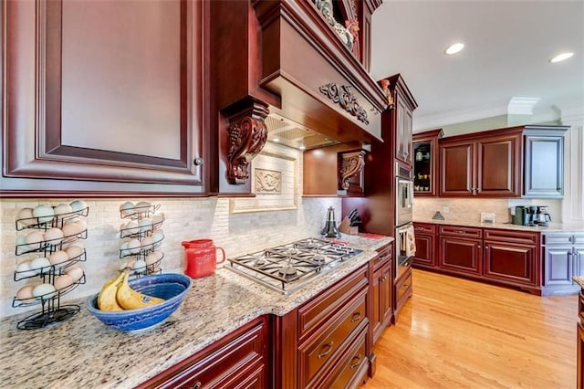 kitchen with custom range hood, light stone countertops, ornamental molding, light hardwood / wood-style floors, and stainless steel appliances