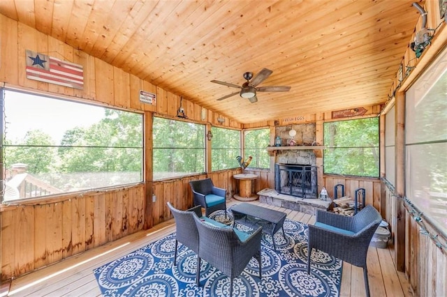 sunroom with ceiling fan, wooden ceiling, a stone fireplace, and vaulted ceiling