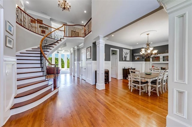 entryway with a notable chandelier, crown molding, light hardwood / wood-style floors, and ornate columns