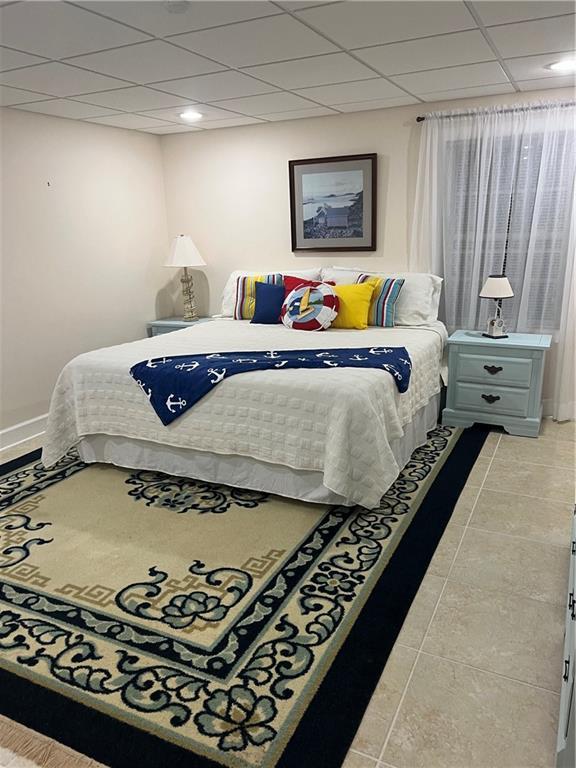 bedroom featuring a paneled ceiling, baseboards, and light tile patterned floors