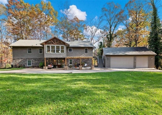 back of property featuring a garage, stone siding, an outbuilding, stairs, and a yard