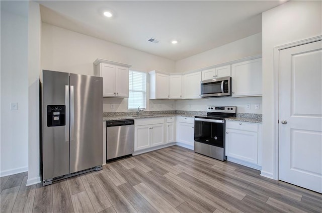 kitchen with white cabinetry, appliances with stainless steel finishes, and light stone counters