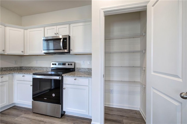 kitchen with appliances with stainless steel finishes, light stone countertops, wood-type flooring, and white cabinets