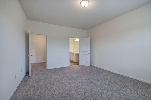 unfurnished bedroom featuring light carpet and ensuite bath