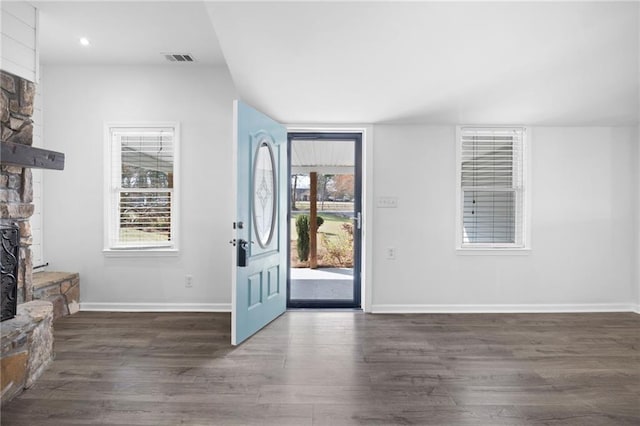 entrance foyer featuring a stone fireplace, dark wood-type flooring, visible vents, and a wealth of natural light