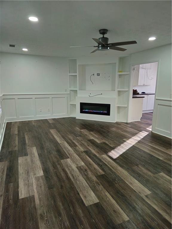 unfurnished living room featuring dark wood-style floors, visible vents, a glass covered fireplace, and a decorative wall