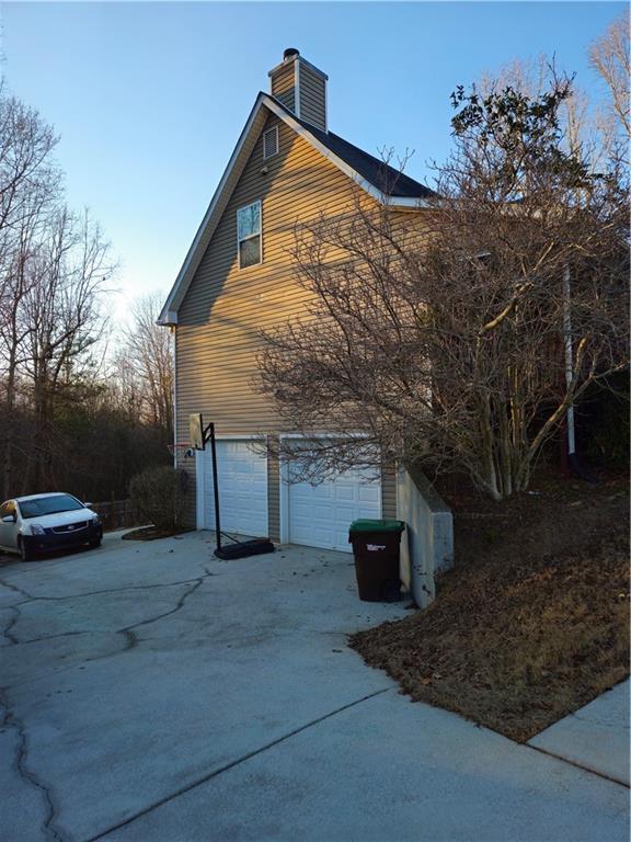 view of side of home featuring a chimney, an attached garage, and concrete driveway