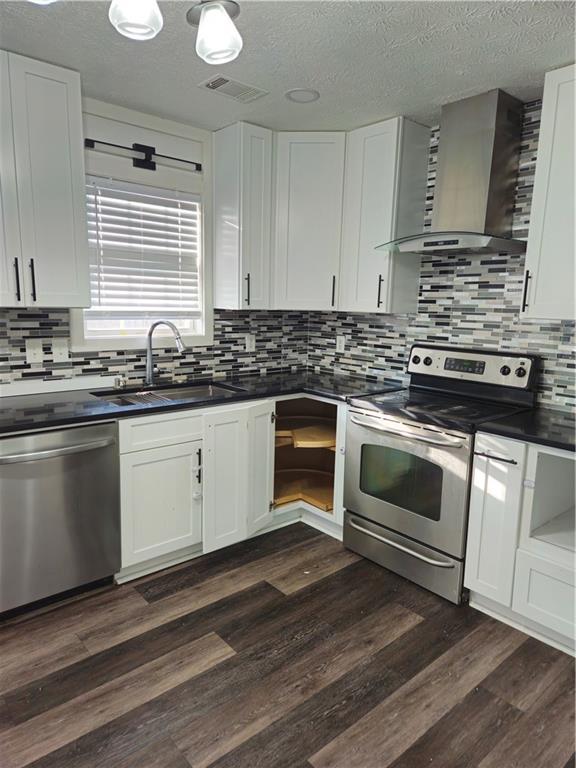 kitchen featuring visible vents, a sink, dark wood-type flooring, appliances with stainless steel finishes, and wall chimney exhaust hood