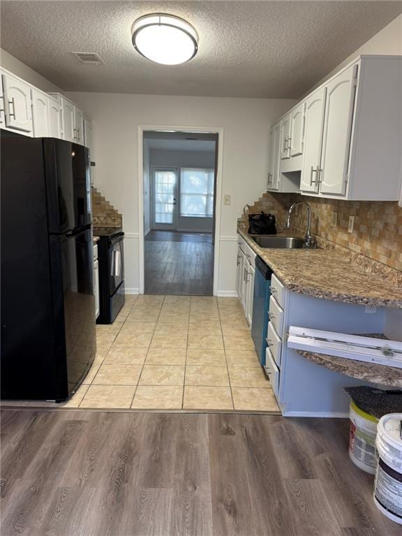 kitchen with white cabinets, black appliances, light wood-style floors, and a sink