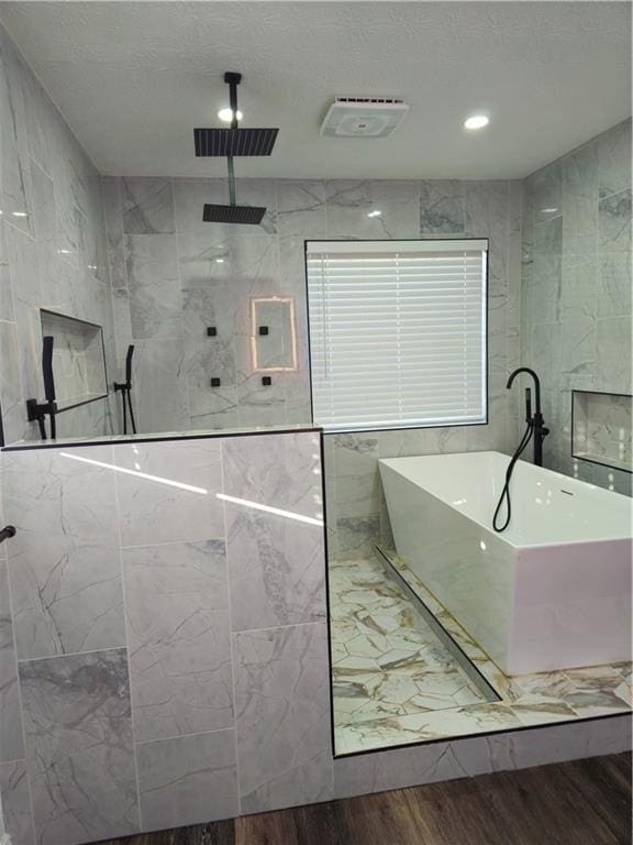 full bath with visible vents, walk in shower, a freestanding bath, wood finished floors, and tile walls