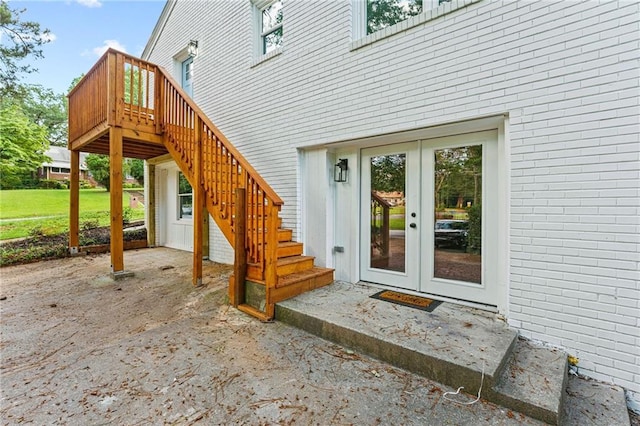 view of exterior entry featuring french doors, brick siding, and a deck