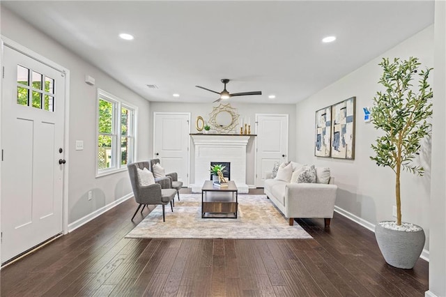 living area featuring baseboards, a fireplace with raised hearth, dark wood-type flooring, and recessed lighting