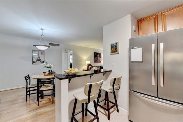 kitchen featuring pendant lighting, a breakfast bar area, stainless steel refrigerator, and kitchen peninsula