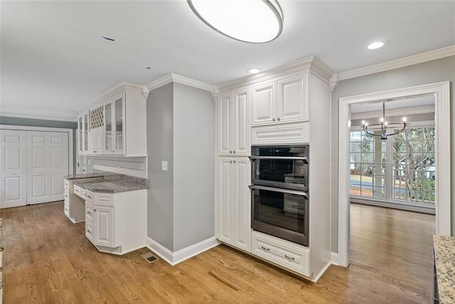 kitchen featuring crown molding, white cabinetry, black double oven, and light stone countertops