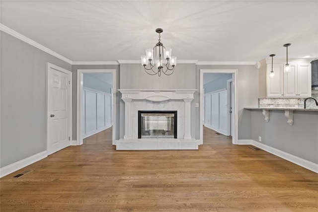 unfurnished living room with a high end fireplace, light wood-type flooring, a chandelier, and ornamental molding