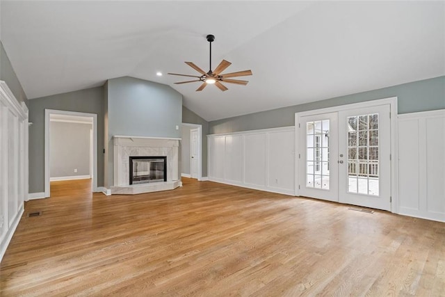 unfurnished living room with a high end fireplace, french doors, ceiling fan, light hardwood / wood-style floors, and lofted ceiling