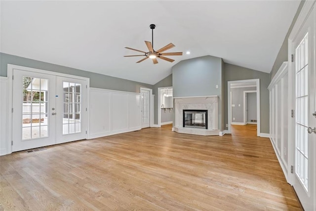 unfurnished living room featuring french doors, vaulted ceiling, ceiling fan, light hardwood / wood-style flooring, and a fireplace