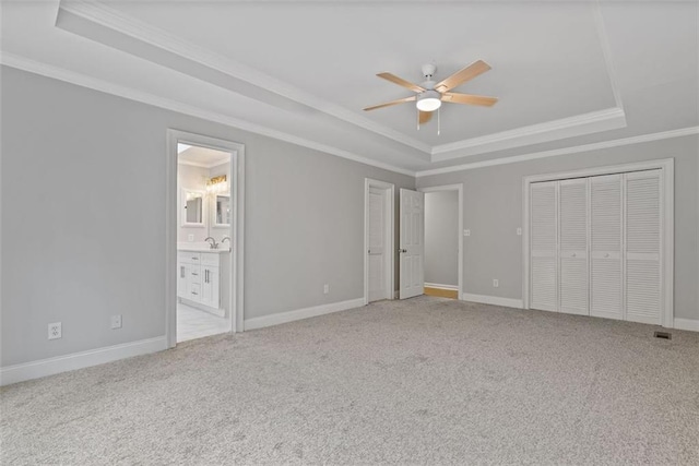 unfurnished bedroom with ensuite bath, ceiling fan, ornamental molding, a tray ceiling, and light colored carpet