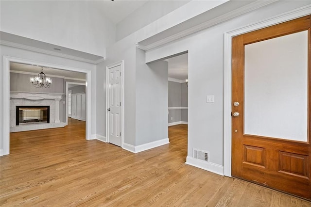 foyer entrance with a chandelier, ornamental molding, a fireplace, and light hardwood / wood-style flooring