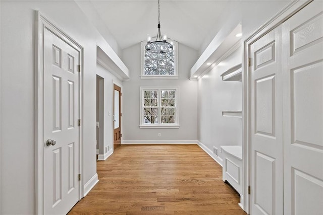 hallway featuring light hardwood / wood-style floors, vaulted ceiling, and an inviting chandelier