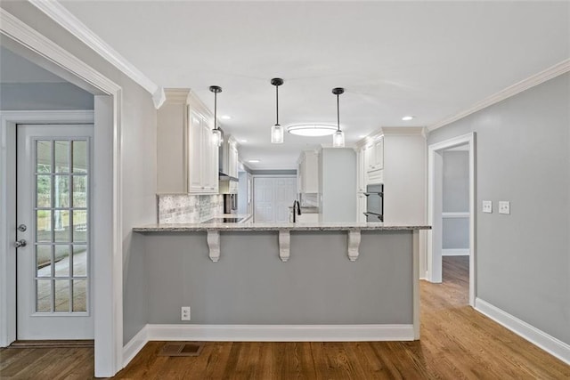 kitchen featuring hanging light fixtures, tasteful backsplash, white cabinetry, kitchen peninsula, and a breakfast bar area