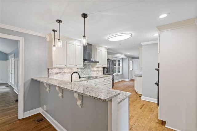 kitchen featuring pendant lighting, white cabinets, wall chimney range hood, kitchen peninsula, and a breakfast bar area