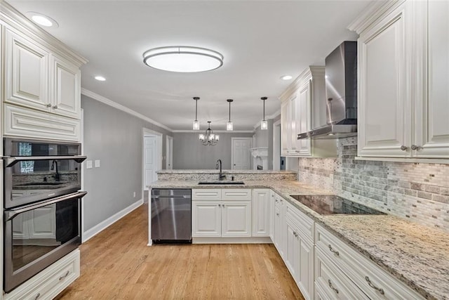 kitchen featuring black appliances, sink, wall chimney exhaust hood, decorative light fixtures, and kitchen peninsula