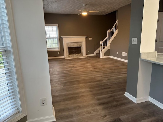 unfurnished living room with dark hardwood / wood-style flooring, ceiling fan, a premium fireplace, and a textured ceiling