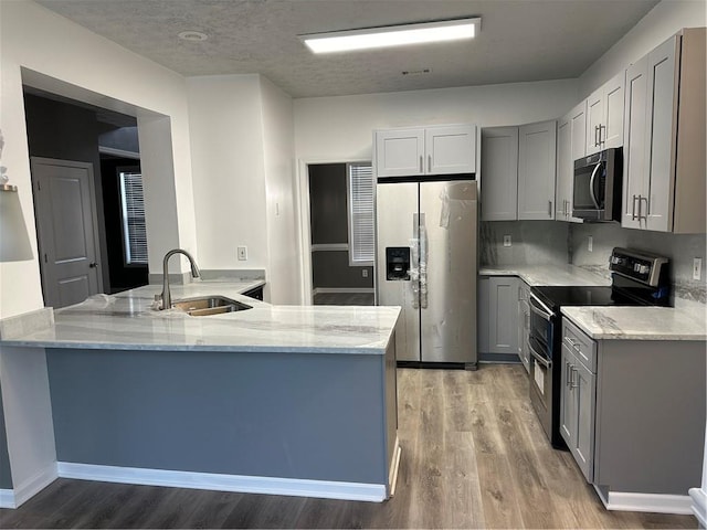 kitchen with sink, gray cabinetry, stainless steel fridge with ice dispenser, kitchen peninsula, and range with two ovens